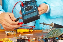 Serviceman checks board of electronic device with a multimeter in service workshop